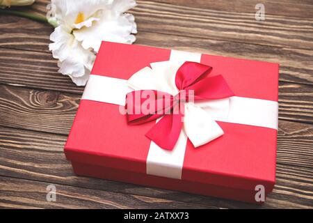 Echte Schachtel mit weißem und rotem Bogen und Band, Blick auf den Valentinstag isoliert auf Holzhintergrund. Flaches Lay. Kopierbereich. Stockfoto