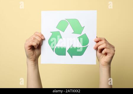 Weibliche Hände halten Blech mit Recycling-Schild vor beigefarbenem Hintergrund, Nahaufnahme Stockfoto