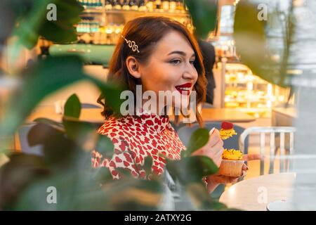 Schöne Brunette-Frau Feiert Allein Den Valentinstag Mit Cupcake Im Stilvollen Café. Selbstverständlichkeit Und Liebe Zu Sich. Stockfoto