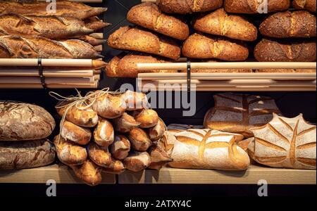 Brotlaibe auf Holzregalen in der Bäckerei in Deutschland. Verschiedene Brotsorten. Leckeres Sauerteig Brot. Gesunde Ernährung. Backwareninnenraum. Stockfoto