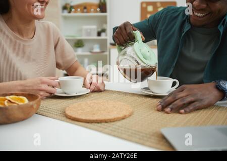Nahaufnahme von jungen Vielvölkerpaaren, die sich gegenseitig genießen und in der Hausküche Kaffee am Tisch trinken Stockfoto