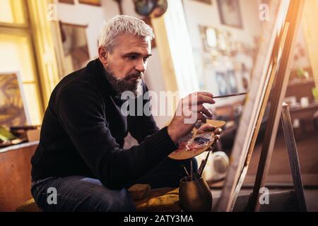 Reifer Mann im Kunststudio auf Leinwand malen. Stockfoto