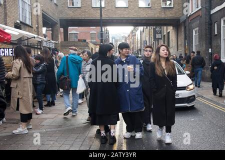 London, Großbritannien, - 23. Dezember 2020, Gruppe modisch gekleideter Menschen, die sich auf der Brick Lane posieren. Ein Mann in einem blauen Mantel. Und zwei in schwarzen Umhängen. Stockfoto