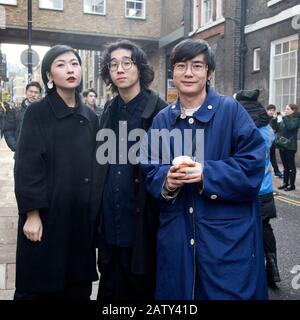 London, Großbritannien, - 23. Dezember 2020, Gruppe modisch gekleideter Menschen, die sich auf der Brick Lane posieren. Ein Mann in einem blauen Mantel. Und zwei in schwarzen Umhängen. Stockfoto