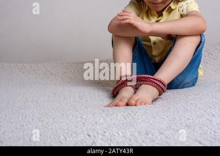 Kleine oy mit Füßen, die mit Seil in emotionalem Stress verbunden sind Stockfoto