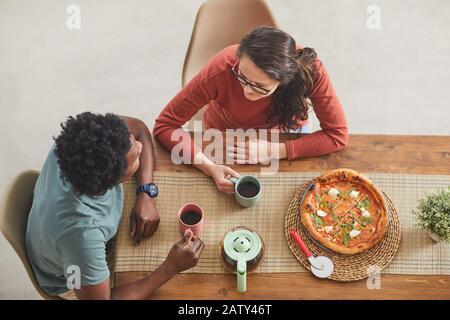 Der Blick auf das junge Paar, das am Holztisch sitzt und zu Mittag essen und Pizza essen und Kaffee trinken Stockfoto