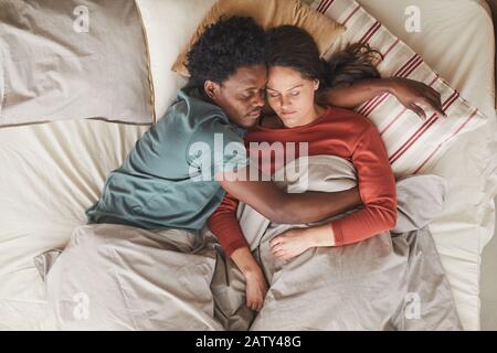 Blick auf das multiethnische Paar, das sich im Schlafzimmer auf dem Bett umarmte und schlief Stockfoto