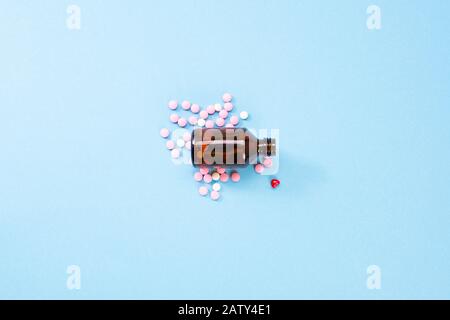 Ein Foto von Tabletten, die aus einer Flasche aus bernsteinfarbtem Glas gegossen wurden. Pharmazeutische Medikamente, Pillen aus dem Herzen auf blauem Hintergrund Stockfoto