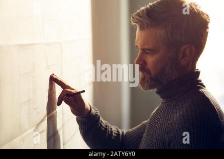 Nahporträt des gutaussehenden Mannes konzentrierte sich auf die Arbeit. Architekt, der im Büro mit Blaupausen arbeitet. Ingenieur skizziert ein Bauprojekt. Archit Stockfoto