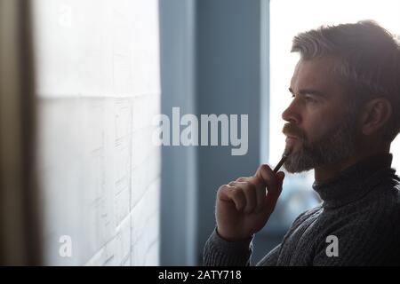 Nahporträt des gutaussehenden Mannes konzentrierte sich auf die Arbeit. Architekt, der im Büro mit Blaupausen arbeitet. Ingenieur skizziert ein Bauprojekt. Archit Stockfoto