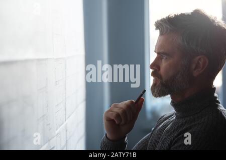 Nahporträt des gutaussehenden Mannes konzentrierte sich auf die Arbeit. Architekt, der im Büro mit Blaupausen arbeitet. Ingenieur skizziert ein Bauprojekt. Archit Stockfoto