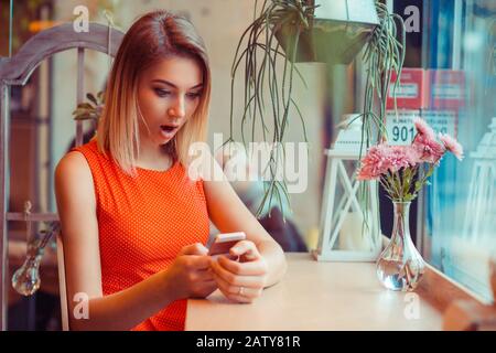 Schlechte Nachrichten. Portrait einer schockierten besorgten Frau, die zu Hause oder im Café ein Smartphone am Tisch neben dem Fenster betrachtet Stockfoto