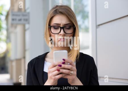 Nachricht wird upsetting. Vorderansicht eines schweren traurigen depressiven Mädchens, das eine Telefonnachricht auf der Straße überprüft. Mixed Race modernes Modell in schwarzen Bussen Stockfoto