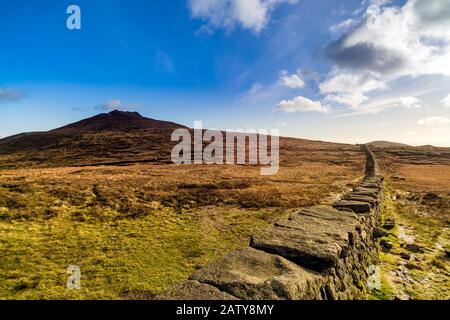 Mourn Wall am Ufer des Berges Slieve Donard mit blauem Himmel, weißen Wolken und Sonnenlicht. Mourne Mountains Range in Nordirland Stockfoto