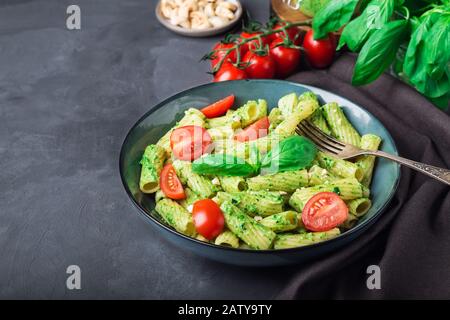 Frische hausgemachte Tortiglioni-Pasta mit veganer Pesto-Sauce, Cashew-Nüssen und Kirschtomaten auf grauem Betongrund. Stockfoto