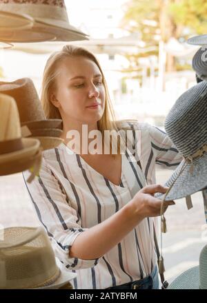 Hübsche Frau, die sich im Urlaub für einen Hut im Geschäft entscheidet. Stockfoto