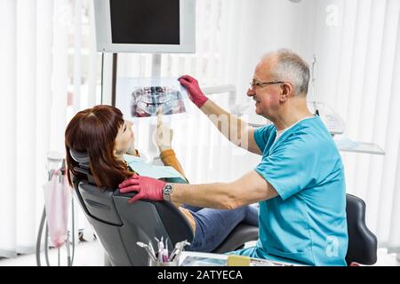 Leitender männlicher Zahnarzt im Zahnbüro, der mit dem jungen Mädchen spricht und sich auf die Behandlung vorbereitet. Röntgenbild wird untersucht. Stockfoto
