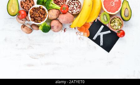 Lebensmittel, die natürliches Kalium enthalten. K: Kartoffeln, Pilze, Banane, Tomaten, Nüsse, Bohnen, Brokkoli, Avocados. Draufsicht. Auf weißem Holzhintergrund. Stockfoto