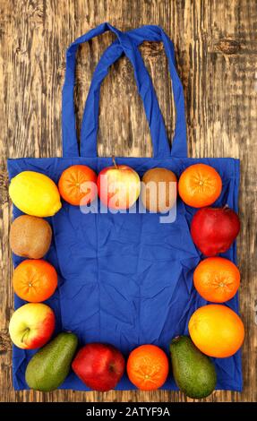 Umweltfreundliche Baumwolltasche in klassischer blauer Farbe mit Obst vor Holzhintergrund. Stockfoto