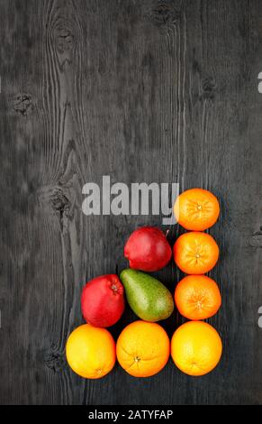 Reife Orangen, Mandarinen, Äpfel, Avocados liegen auf einer alten schwarzen Holzoberfläche, flacher Lay, Bild mit Kopierraum. Stockfoto