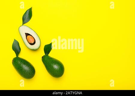 Frische reife organische grüne Avocados und Hälften mit Blatt auf farbigem gelbem Hintergrund, Top-View-Sommernahrungskonzept mit Kopierraum für Ihren Text. Minimal Stockfoto