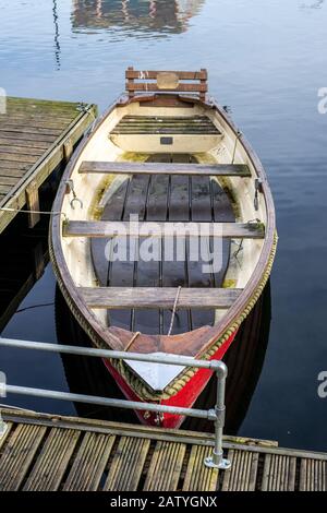 Ein altes leeres Holzruderboot fesselte auf einem Holzsteg auf ruhigem Wasser Stockfoto