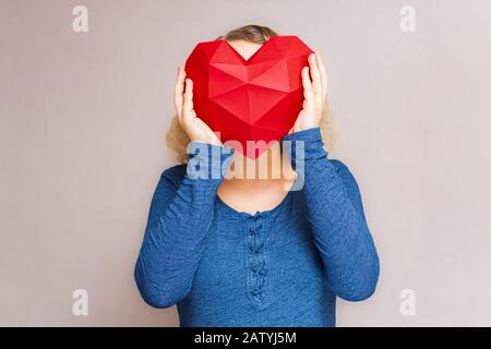 Junge Frau, die ein polygonales rautenförmiges rotes Herz vor dem Kopf hält Stockfoto