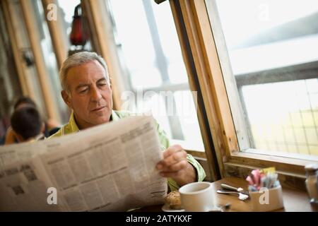 Reifer Mann liest eine Zeitung, während er in einem Café sitzt. Stockfoto