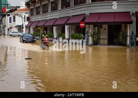 Georgetown, Penang, Malaysia - 5. November 2017: Einheimischer, der nach starkem Regen mit dem Motorrad auf der braun überfluteten Straße unterwegs ist Stockfoto