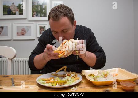 Ein Mann, der zu Hause sitzt und einen Dönner Kebab und Chips zum Mitnehmen mitnimmt, Großbritannien Stockfoto