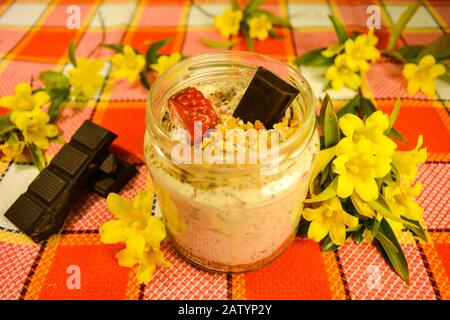 Ein süßes Dessert zur Geburtstagsfeier, Stracciatella Käsekuchen in einer Tasse mit Schokolade, Erdbeere und Haselnuss-Dekoration, Plätzchen zerbröckelter Unterlage. D Stockfoto