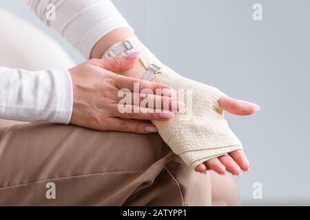 Frau, die ihr gewickeltes schmerzhaftes Handgelenk mit einem flexiblen elastischen, unterstützenden orthopädischen Verband berührt, nachdem sie Sport oder Verletzung nicht erfolgreich war, Nahaufnahme. Stockfoto