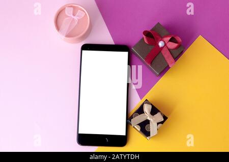 Telefonbildschirm und Geschenke auf farbigem Hintergrund. Minimales Konzept. Flaches Layout. Draufsicht.Online-Angebote und Rabatte. Weihnachtsgeschenke und Überraschungen Stockfoto