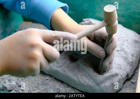 Kind, das Fossil-, Mineral- und Schatzgräbenspiel spielt. Das Kind verwendet Werkzeuge, wie z. B. einen Hammer. Stockfoto