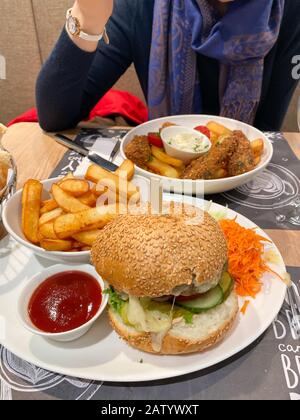 Frau, die neben einer reichhaltigen Portion mit Burger und Pommes frites köstliche Fisch und Pommes isst Stockfoto