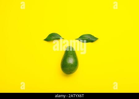 Kreatives Gesicht aus Avocado und grünen Blättern. Minimaler Stil Sommerfrucht flach lag Avocado auf gelbem Farbhintergrund. Stockfoto