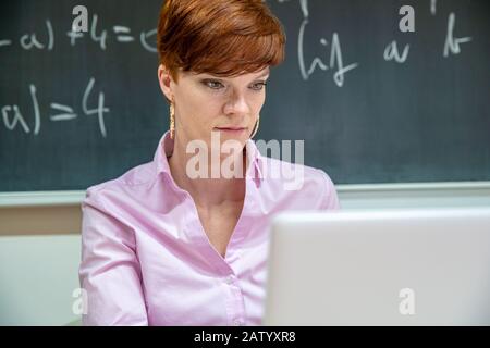 Der junge Lehrer überprüft Hausaufgaben auf seinem Laptop in einer Grundschule im Klassenzimmer Stockfoto