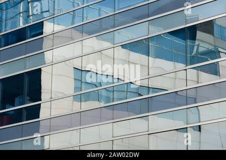 Reflektierendes Gebäude, in dem die umliegenden Gebäude reflektiert werden. Bild von parallelen und senkrechten Linien in bläulichen Tönen. Puerto Madero, Buenos Aire Stockfoto