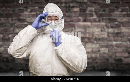 Chinesischer Mann Mit Hazmat-Anzug, Schutzbrille und Maske mit Brick Wall Hintergrund. Stockfoto