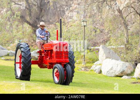 Gutaussehender Mann mit Sonnenbrille, der den Traktor fährt, um auf dem Bauernhof zu arbeiten Stockfoto