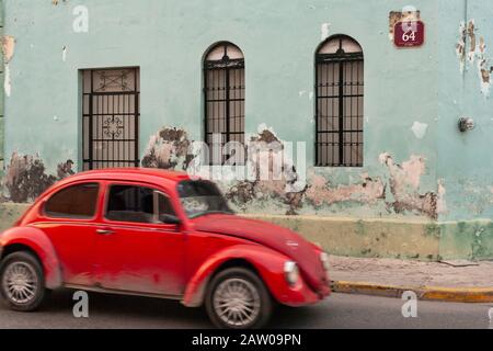 Ein klassischer roter Volkswagen Käfer fährt von einem mintgrünen Gebäude an der Calle 64 in Merida, Yucatan, Mexiko. Stockfoto