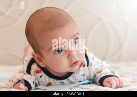 Portrait von 2 Monate alt liebenswert Baby junge mit großen blauen Augen und langen Wimpern. Nettes Baby liegt auf dem Bauch und schaut weg mit überrascht