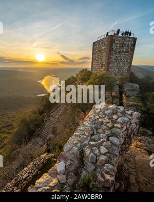 Eine Outdoor-Frau Touristen genießen die erstaunliche Aussicht während des Sonnenuntergangs von Extremadura Landfelder, es Wälder und Tajo Fluss von der atemberaubenden Burg Monfragûe Stockfoto