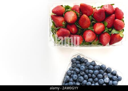 Erdbeeren und Blaubeeren in Kunststoffbehältern liegen auf weißem Hintergrund, Ansicht von oben Stockfoto