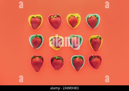 Erdbeeren in bunten, herzförmigen Kunststoffformen schließen sich auf rotem Hintergrund, Ansicht von oben Stockfoto