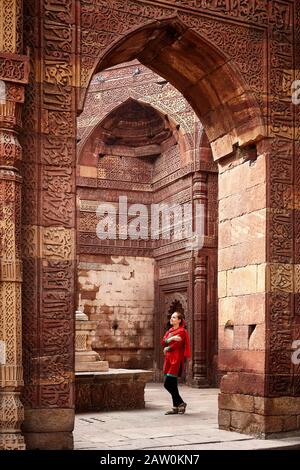 Frau in rotem Kleid an geschnitzten Bögen und Grabtor im Qutub Minar Komplex in Neu-Delhi, Indien Stockfoto