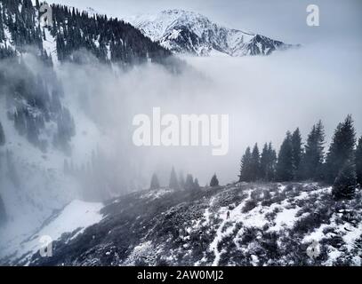 Kleiner Mann mit rotem Rucksack in den Winterbergen im Nebel. Luftdrohne erschossen. Stockfoto