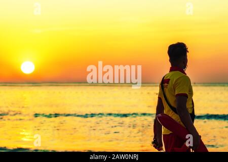 Ein Bademeister am Strand, der in gelb-roter Uniform am Meer während des Sonnenuntergangs in einem Strand von Dubai in den Vereinigten Arabischen Emiraten gekleidet ist. Stockfoto