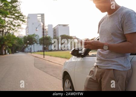 Junge Mann steht in der Nähe des elektrischen Auto und schaut auf dem Smartphone. Der mietwagen wird der Ladevorgang an der Ladestation für Elektrofahrzeuge. Ca Stockfoto