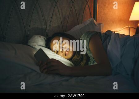Mädchen benutzt ein Handy, während sie im Bett liegen und lächeln. Stockfoto